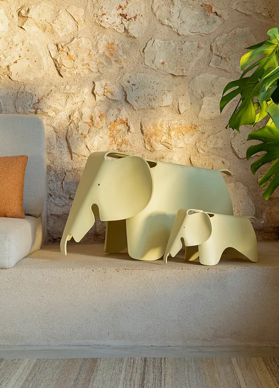Zwei Eames Elephant aus hellgrünem Kunststoff auf Steinbank vor Natursteinwand neben Zimmerpflanze.